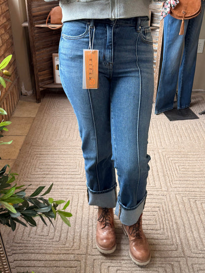Front-seam medium-wash jeans with cuffed bottoms and leather-brown lace-up shoes.