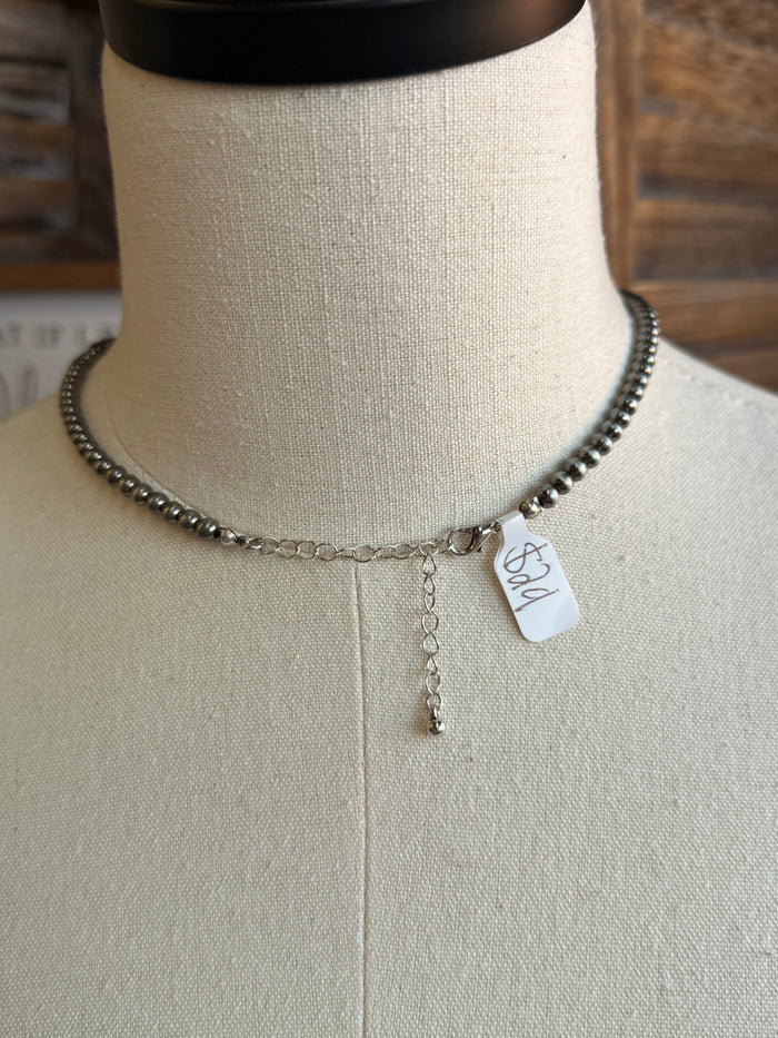 Silver-tone beaded necklace with dangling charm and attached tag