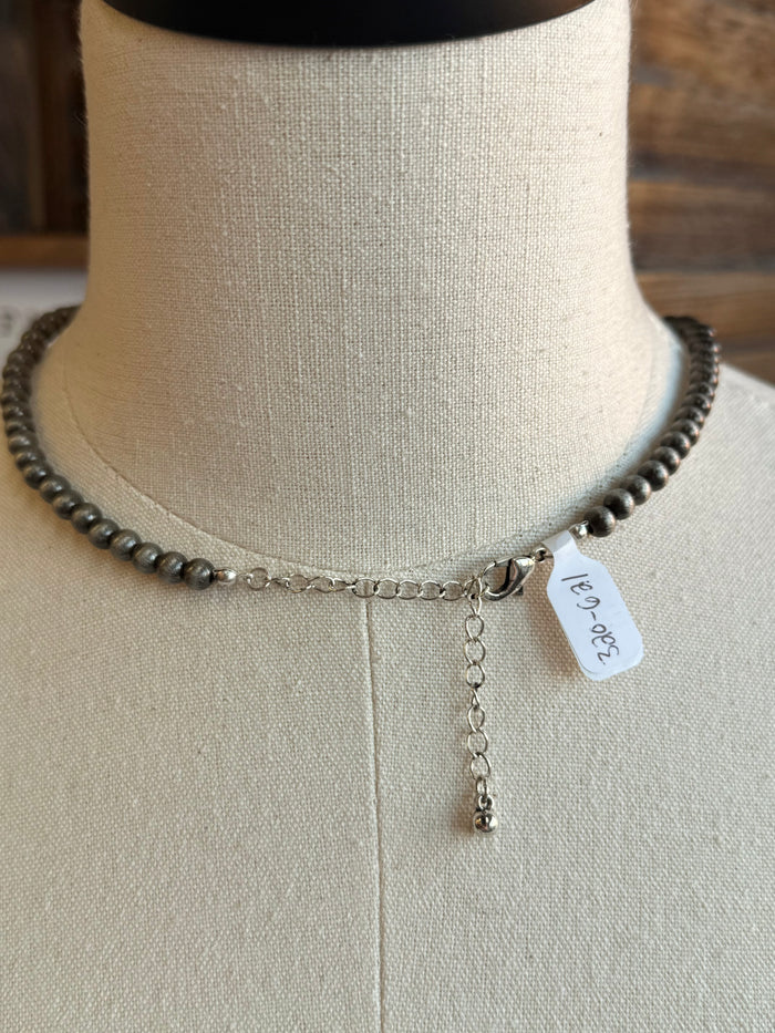 Close-up of silver pearl bead necklace with small dangling charm and engraved tag