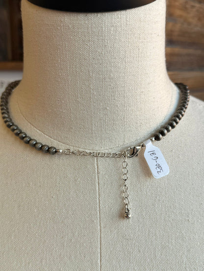 Close-up of silver pearl bead necklace with small dangling charm and engraved tag