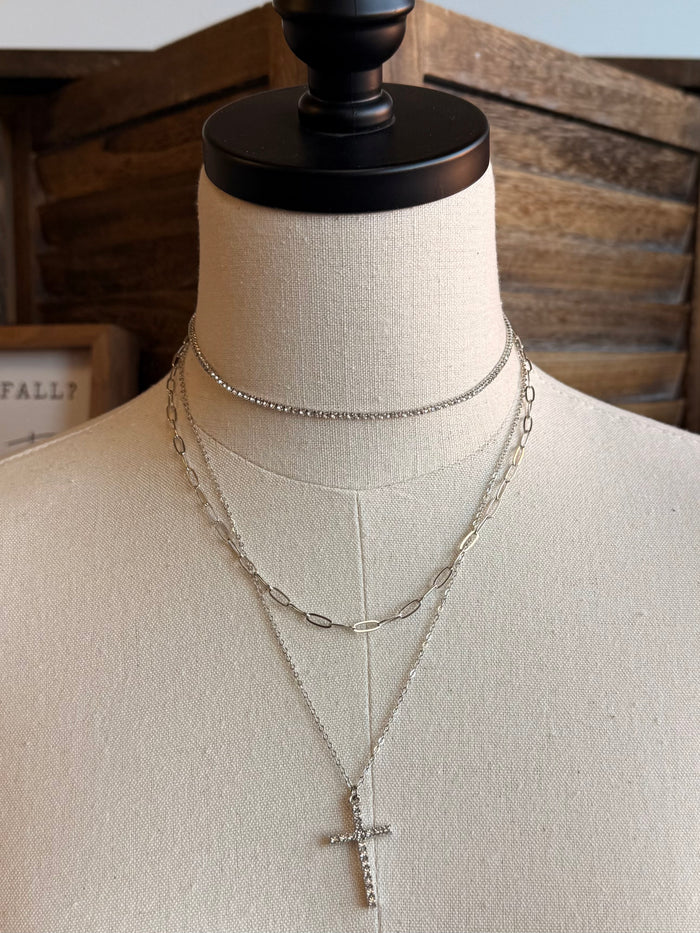 Silver stack necklace with cross pendant and double-chain layers on a mannequin