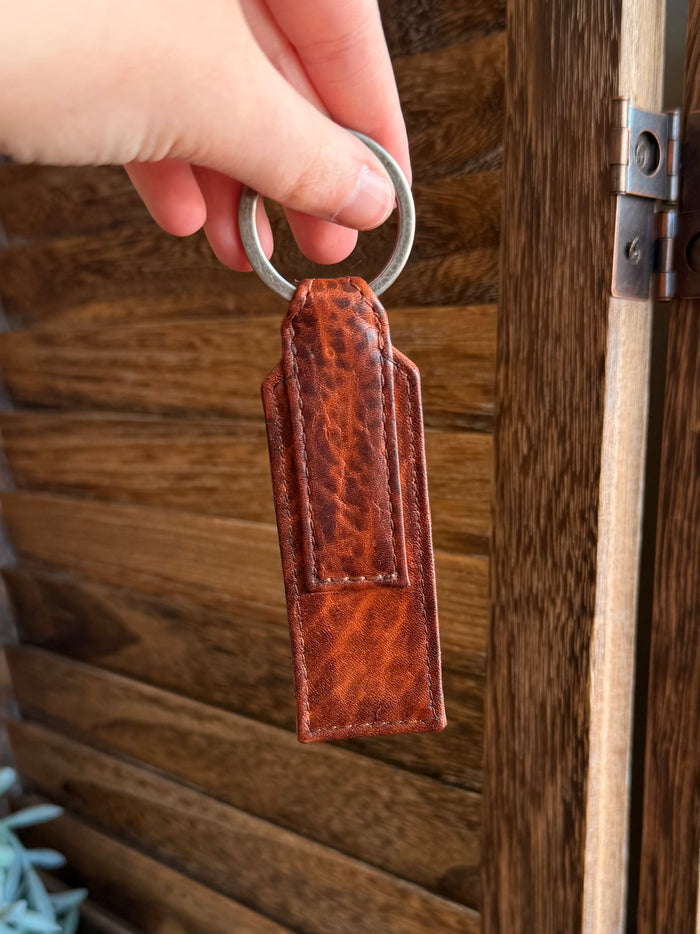 Rusty brown textured leather keychain tag with curved top loop and key ring, side view