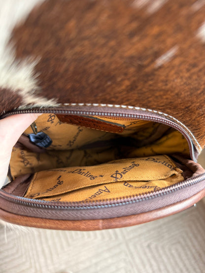 Open cowhide sling bag showing tan printed lining and zippered interior pocket