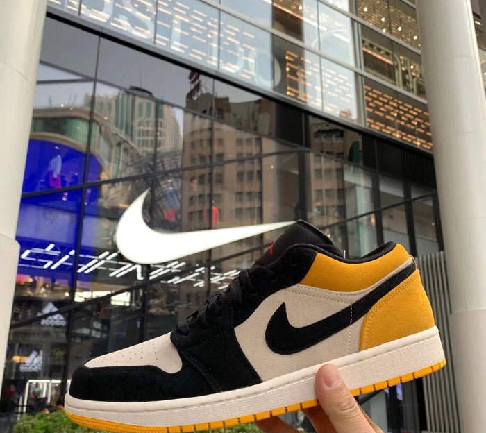 Air Jordan 1 sneaker held up, black with sail panel and gold Nike swoosh
