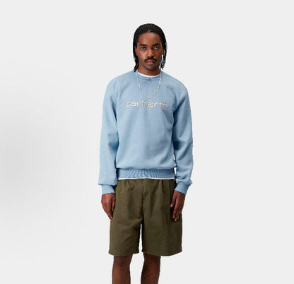 Carhartt WIP crewneck sweatshirt, light blue, worn with long sleeves and chest logo