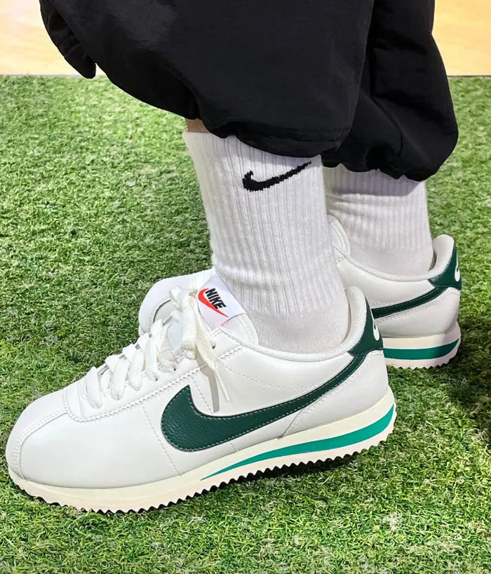 Cortez sneakers on green grass, white uppers with green swoosh accents