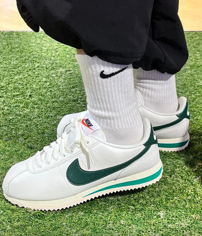Cortez sneakers on green grass, white uppers with green swoosh accents