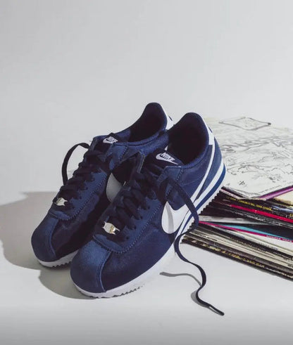 Dark blue lace-up sneakers with white swoosh, shown with extra shoes nearby
