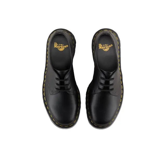 Black lace-up shoe pair with Dr. Martens logo on tongue and yellow welt stitching