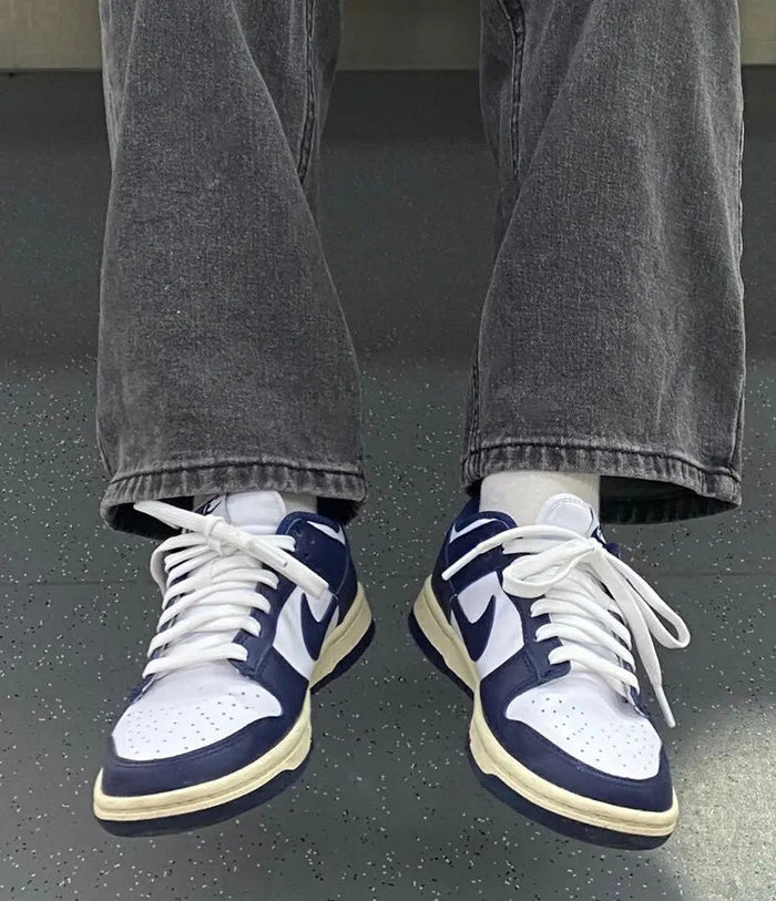 Low-top sneakers on feet with white laces, navy uppers, and cream soles