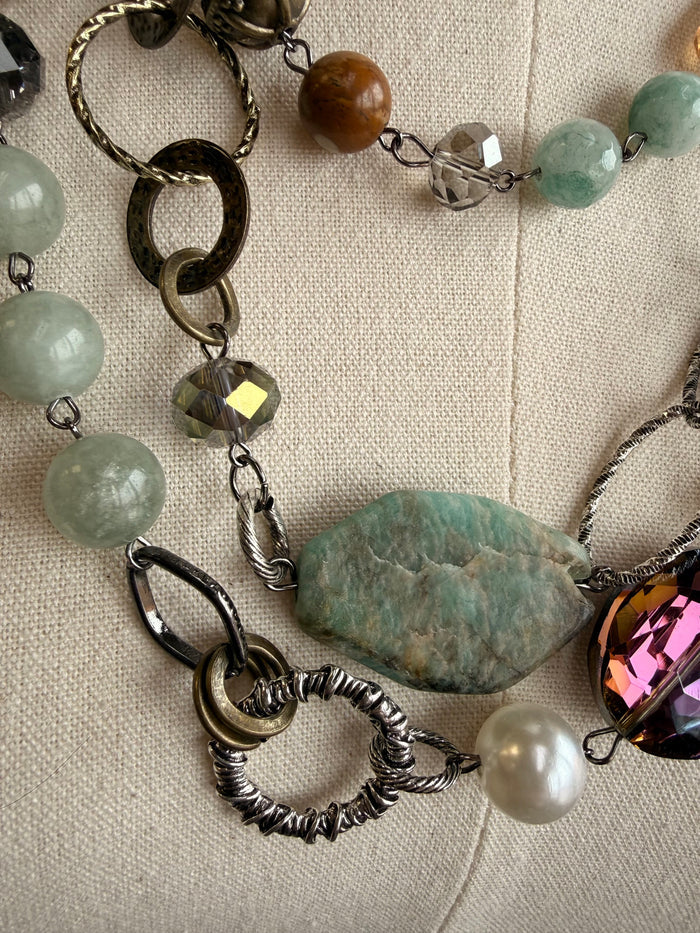 Layered necklace close-up with blue-green and pearl-like beads, faceted amber stone, silver links