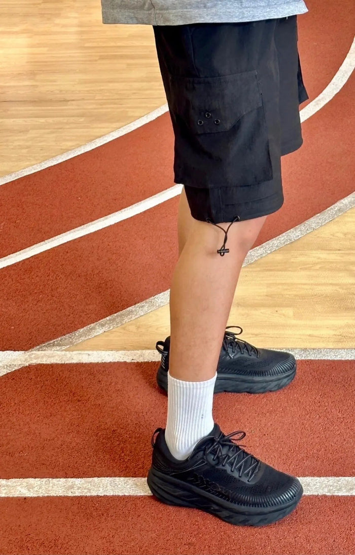 Black running shoe on foot with white crew socks and cuffed pants