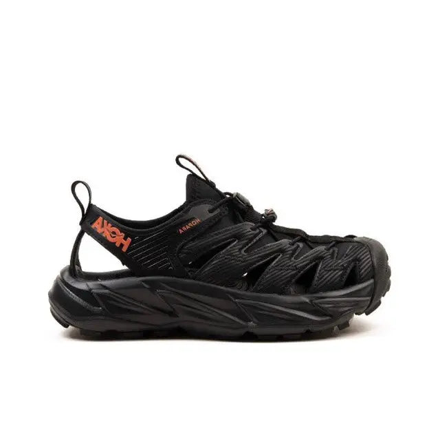 Trail shoe side profile, black upper with orange logo accents and thick sole