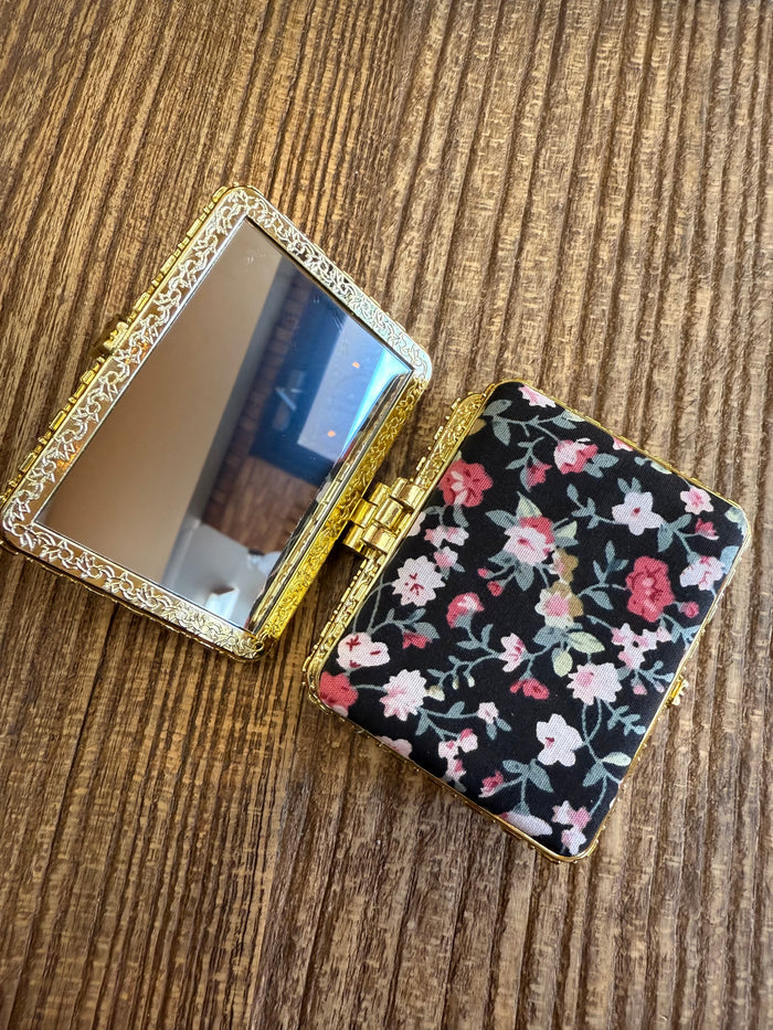 Black floral mirror compact with hinged case and round mirror, gold-tone trim