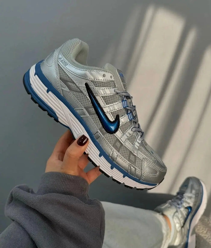 Nike running shoe held in hand, silver upper with blue Swoosh and lace-up closure.