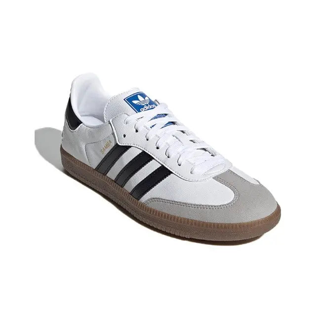 White Adidas Samba vegan sneakers with black stripes, blue tongue label, and gum sole.