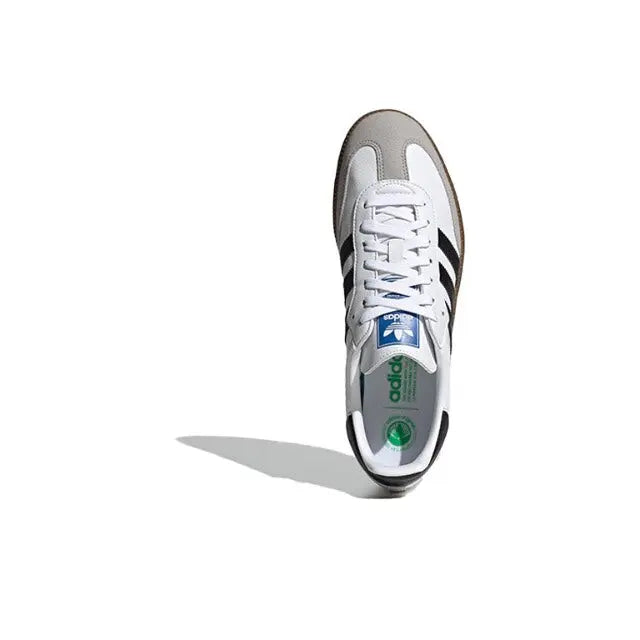 Top view of Adidas Samba vegan sneakers with white upper, black stripes, and blue tag.