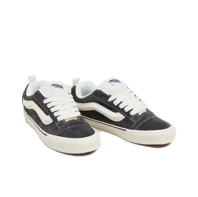 Vans Knu Skool low-top sneakers, angled view; dark uppers with white side stripe and laces