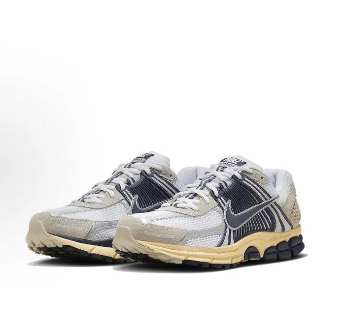 Nike running sneaker pair in light gray with navy swoosh and tan midsole, side stripes